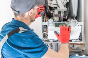 A technician wearing red gloves repairing a furnace that's experiencing problems
