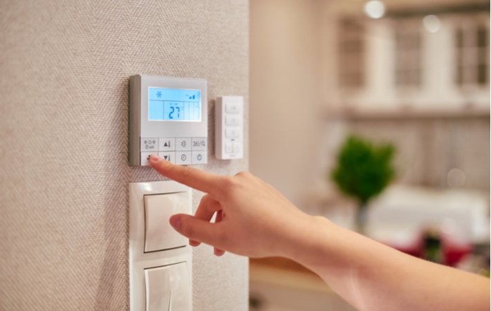 A person reaching to touch their thermostat to adjust the temperature in their home.