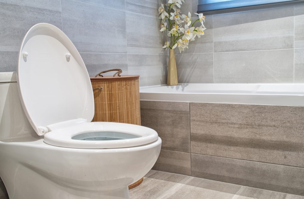 A toilet with open lid in a modern bathroom with natural light entering through the window above the bathtub.