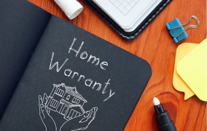 A black notebook reading the words "home warranty" with a drawing of two hands carefully holding a house underneath