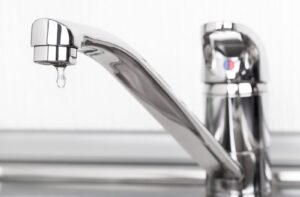 A close up of a silver faucet leaking water slowly