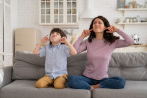 A woman and child sitting on a couch and covering their ears due to a loud sound.