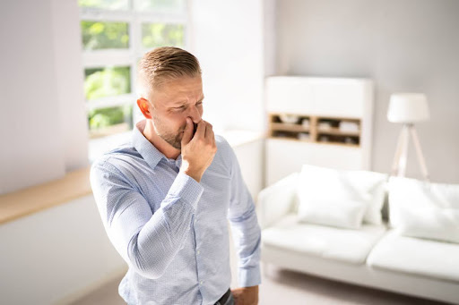 A man holding his nose in a house due to a bad smell.