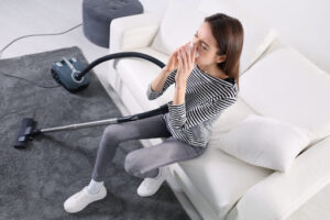 A woman sneezing as she vacuums a rug.