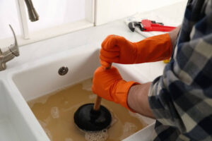 A man using a plunger in a sink that's backed up with dirty water.