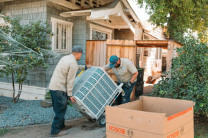 Lee's AC technicians moving new air conditioner into a house.