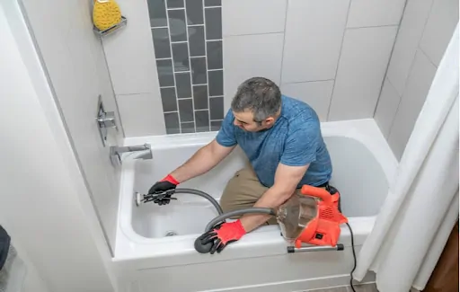 A plumber cleaning a bathtubs drain with a plumbers snake