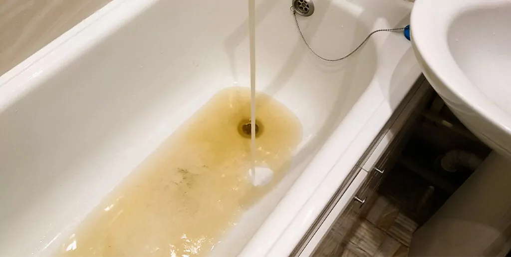 Bathtub filling with brown water flowing from faucet.