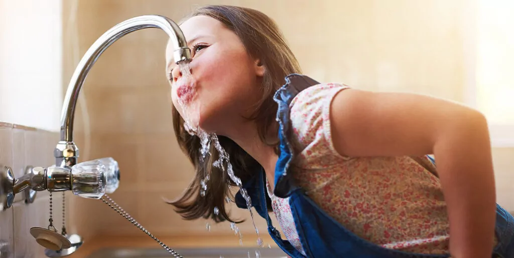 Young woman drinking clean tap water from kitchen faucet.