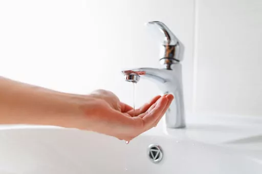 A hand catching the water coming out of a sink faucet. The water is only a small trickle.