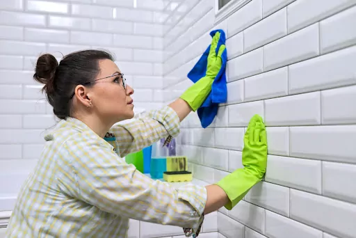 Woman scrubbing bathroom tiles because of mold growth.