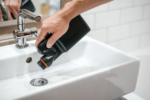 A hand pouring chemical drain cleaner down a bathroom sink drain.